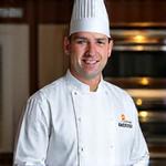 Portrait souriant d'Émile Dubois, co-fondateur et chef pâtissier de Gourmandise Velours, en tenue de chef.